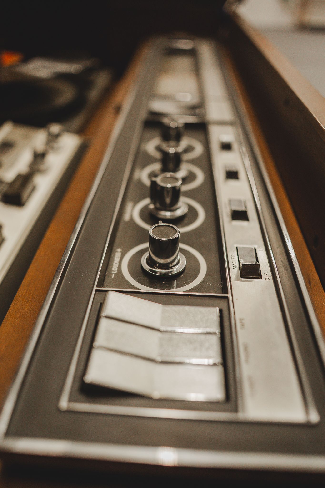 Black knobs and chrome switches on the control panel of a vintage stereo console