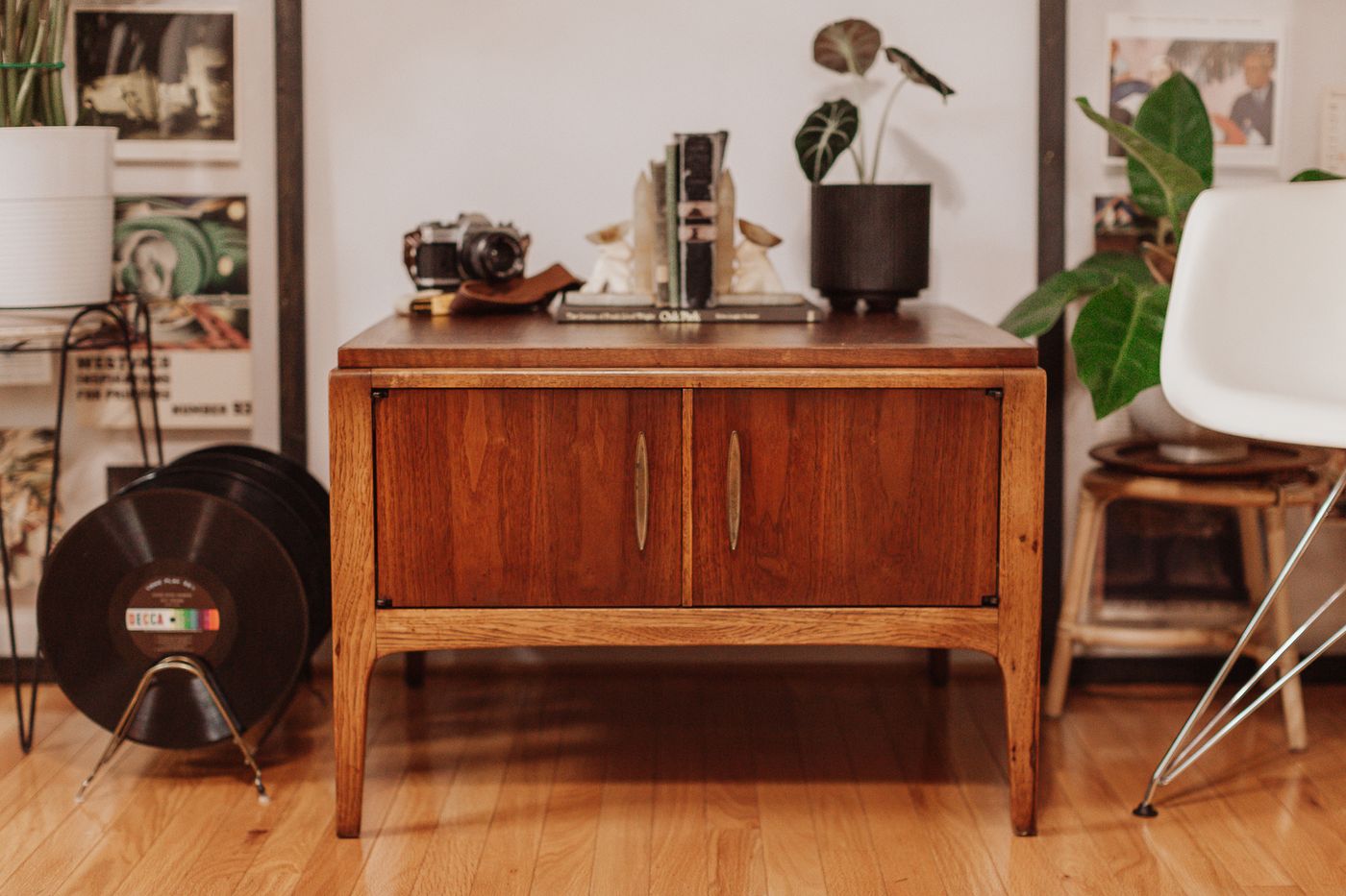 Mid-century wood side table with two doors and brass pulls, styled with a camera, books and plants